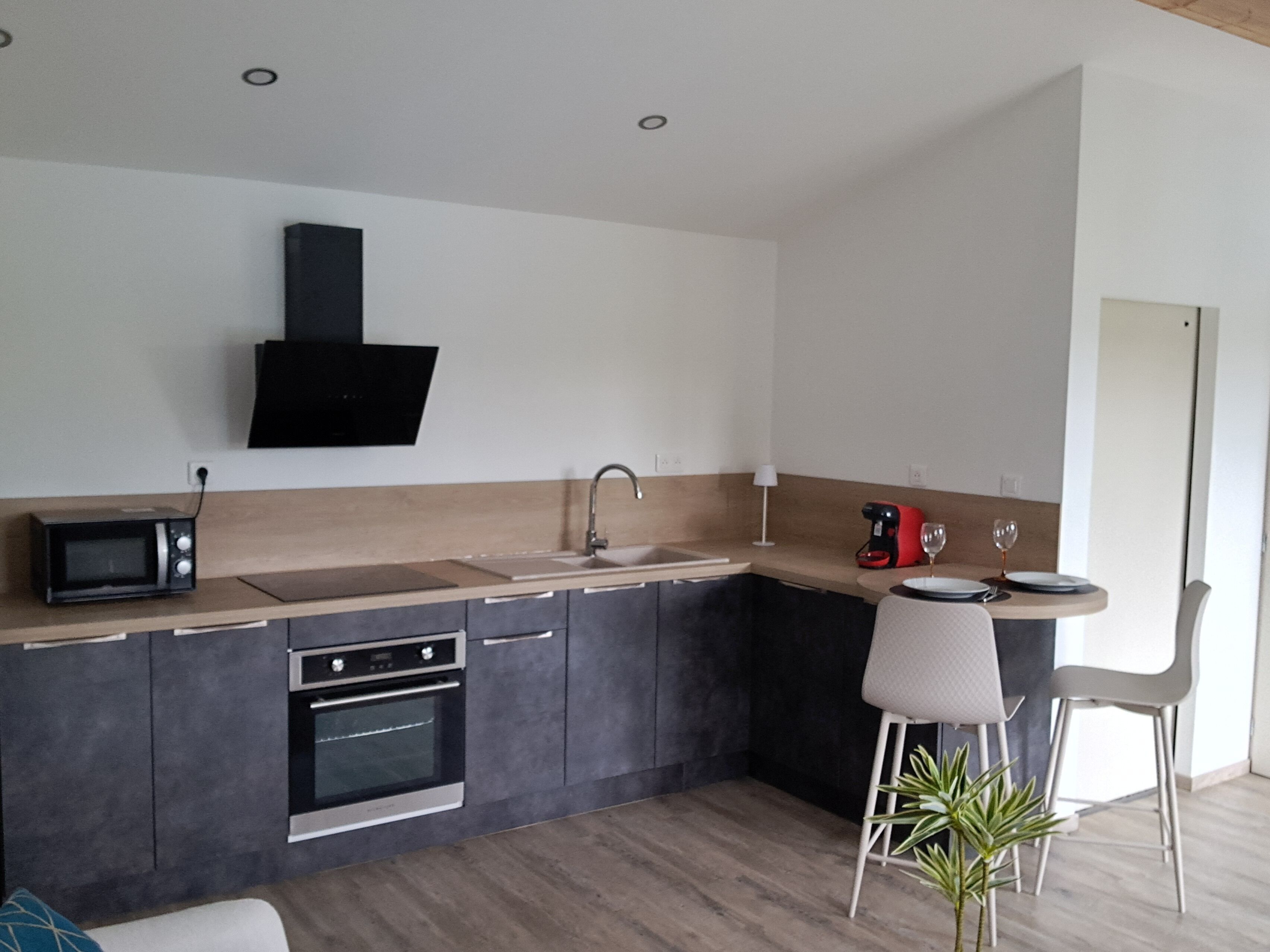 A modern kitchen with a microwave, oven, sink, and a small dining area with a chair and table.