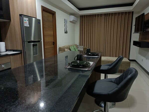 Una cocina moderna con un refrigerador de acero inoxidable, una puerta de madera y un comedor con una mesa lista para dos.