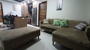 A living room with a sofa, ottoman, and a kitchenette area with a refrigerator. - Comfort in the best area of Santa Cruz—perfect for business travelers and tourists!! (Santa Cruz de la Sierra)