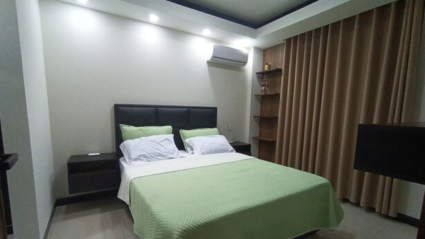 A hotel room with a bed, nightstands, an air conditioning unit, a television, and a curtain. - Comfort in the best area of Santa Cruz—perfect for business travelers and tourists!! (Santa Cruz de la Sierra)