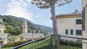 A balcony with a tree, a building with a clock tower, and a mountainous landscape in the background. - Camogli Sea and Valley View by Wonderful Italy (Camogli)