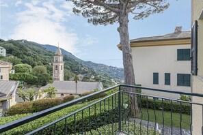 Ein Balkon mit Baum, ein Gebäude mit Uhrturm und eine gebirgige Landschaft im Hintergrund.