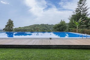 Ein rechteckiger Swimmingpool mit Holzdeck im Vordergrund, umgeben von Grünpflanzen und Bäumen.
