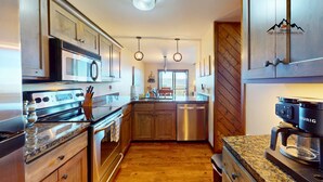 A modern kitchen with stainless steel appliances, wooden cabinets, and a granite countertop. - Crest 200C • Panoramic Views and Huge Shower (Sugar Mountain)