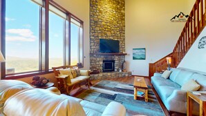 A spacious living room with a stone fireplace, large windows, and a view of the landscape. - Crest 200C • Panoramic Views and Huge Shower (Sugar Mountain)