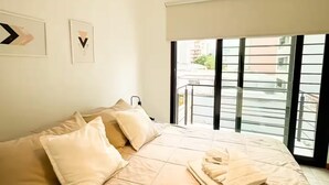 Ein Schlafzimmer mit einem Bett, Kissen, einem Fenster mit Blick und zwei gerahmten Bildern an der Wand.