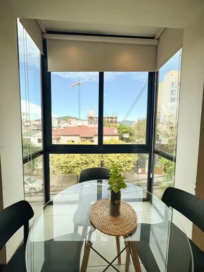 Habitación con una mesa de vidrio, una planta en maceta y vistas a edificios y una grúa en el exterior.
