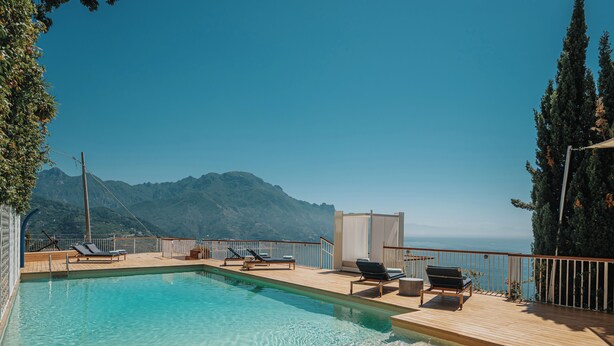 Ein Pool mit Liegestühlen, eine Holzterrasse und Blick auf die Berge.