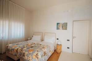 Ein Schlafzimmer mit zwei Betten, einem großen Fenster mit Vorhängen, einer Tür und einem kleinen Wandbild.
