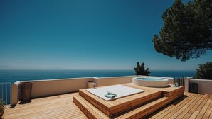 Eine Holzterrasse mit Whirlpool und Liegestuhl mit Blick auf ein Gewässer.
