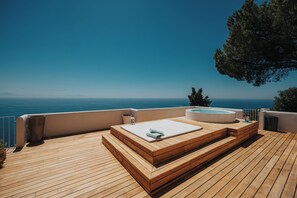 Eine Holzterrasse mit Whirlpool und Liegestuhl mit Blick auf ein Gewässer.