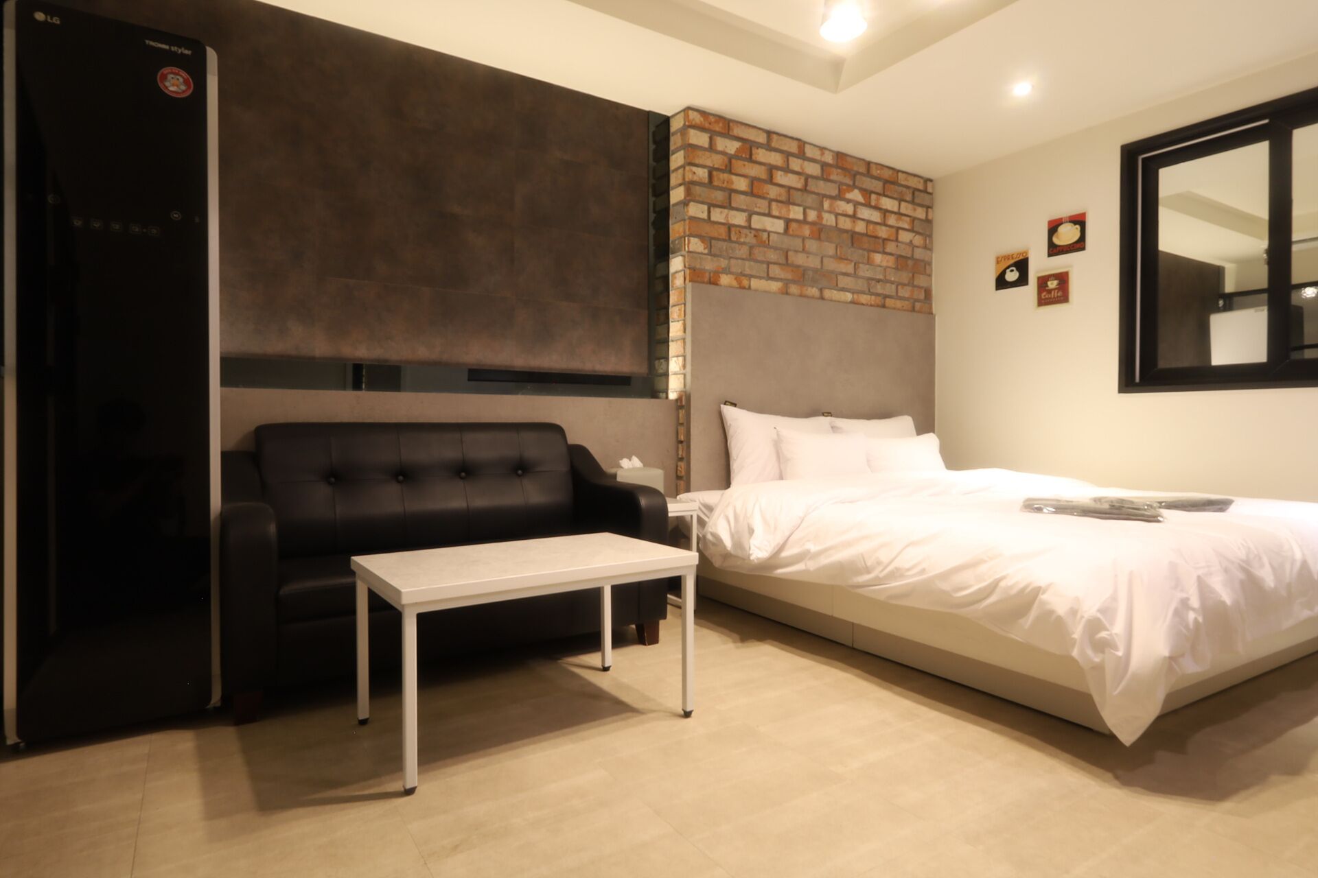 Una habitación de hotel moderna con una cama, un sofá, una mesita y una pared de ladrillo decorativa, además de un espejo.