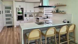 Een moderne keuken met witte kasten, een centraal eiland met barstoelen, een inbouwoven en een roestvrijstalen afzuigkap.