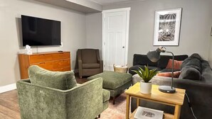 A living room with a green armchair, a wooden dresser, a television, a black couch, and a small table with a plant. - Private 2BR retreat near Zion, Shakespeare and downtown (Cedar City)