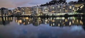 Ein Hotel am Wasserufer mit mehreren Etagen, Balkonen und einem Spiegelbild im ruhigen Wasser.