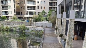 Un paseo marítimo de madera junto a una masa de agua, bordeado por edificios modernos con balcones y fachada de piedra.