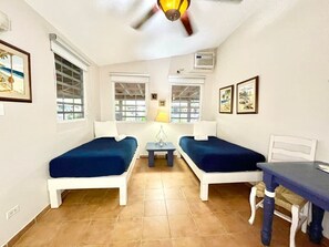 A room with two beds, a small table, a ceiling fan, and a window with blinds. - Villa 14 Flamenco Beachfront Villas (Flamenco)