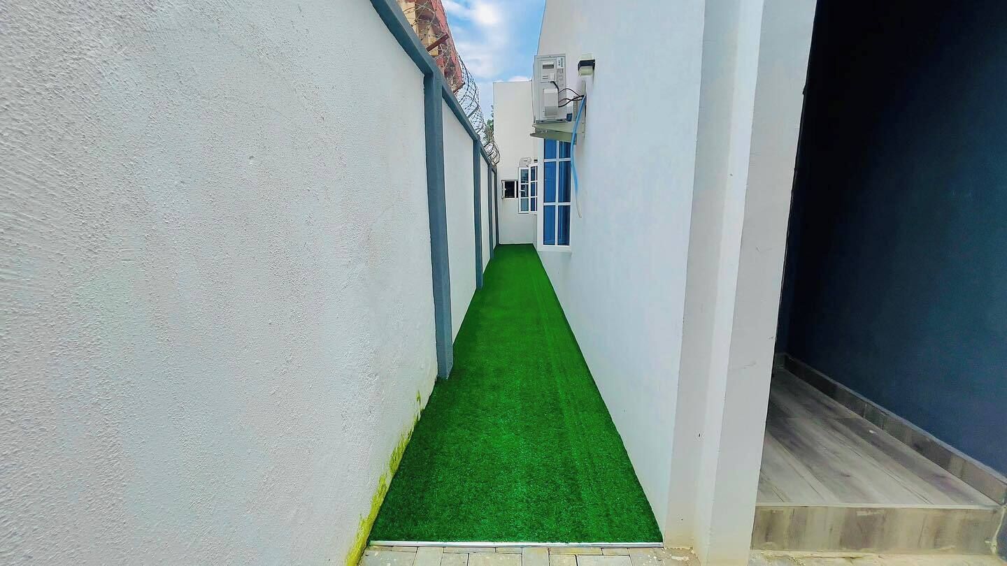 A narrow corridor with artificial green flooring, white walls, and a blue door at the end.