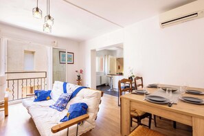 A room with a bed, a dining table set for four, and a kitchen in the background. - House with beautiful rooftop terrace between sea, canal and village (Villeneuve-lès-Béziers)