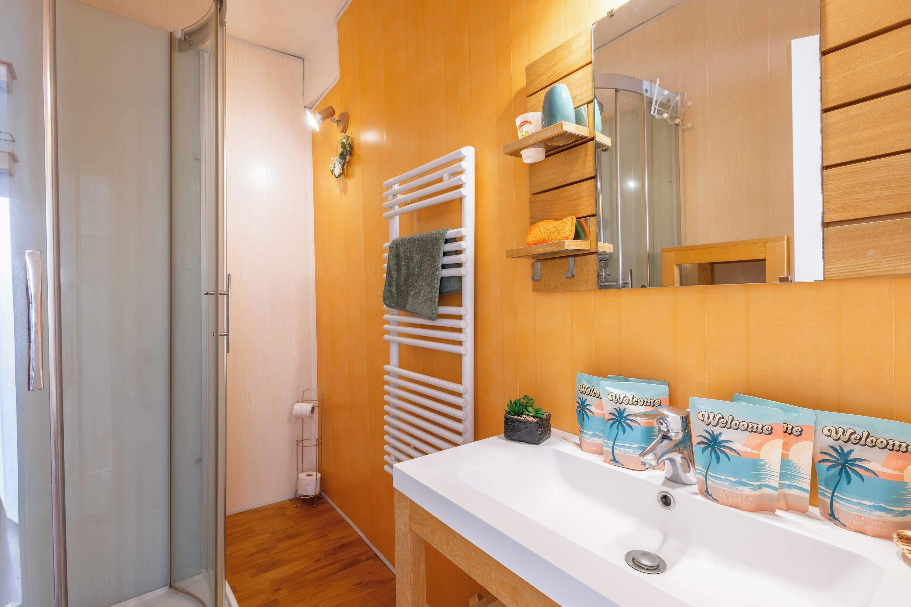 Une salle de bain avec un lavabo blanc, un porte-serviettes, une cabine de douche en verre et un mur en bois.