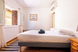 A bedroom with a bed, a wooden nightstand, a framed picture on the wall, and a window with curtains. - House with beautiful rooftop terrace between sea, canal and village (Villeneuve-lès-Béziers)