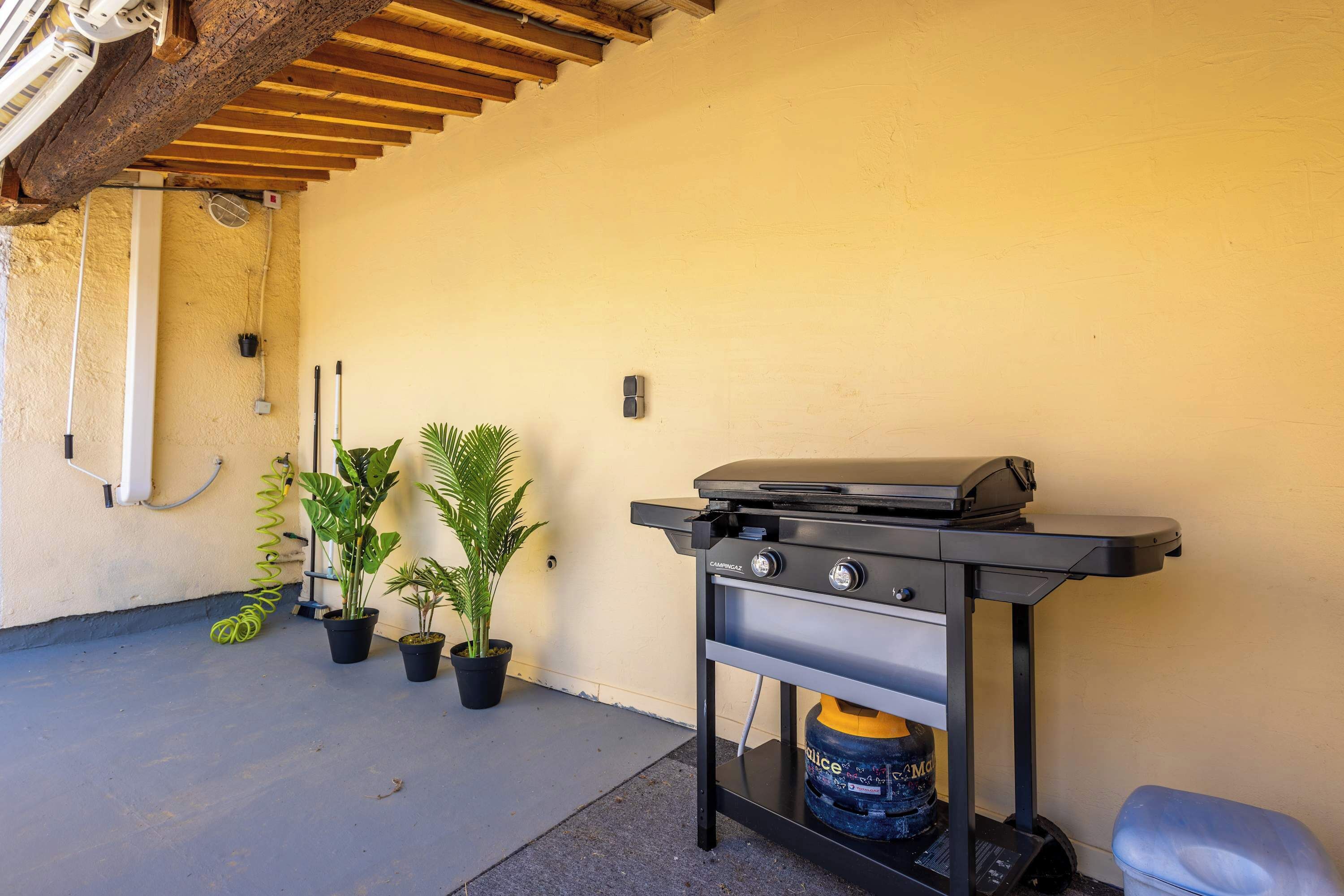 Un barbecue à gaz, des plantes en pot et une structure de plafond en bois.