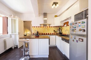 A kitchen with white cabinets, a central island, a stainless steel range hood, and a refrigerator with magnets. - House with beautiful rooftop terrace between sea, canal and village (Villeneuve-lès-Béziers)