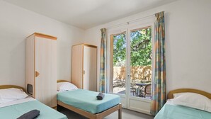 A room with two single beds, a wardrobe, and a sliding glass door to an outdoor area.