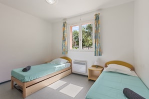Una habitación con dos camas individuales, una ventana con cortinas, un radiador y una mesita de noche con lámpara.