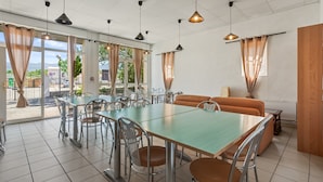 A dining area with a long table and chairs, a sofa, and large windows with curtains.