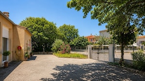 A gravel driveway leading to a gated entrance, surrounded by trees and potted plants.