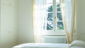 Um quarto com uma cama, uma janela com cortinas e um radiador.