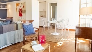 Quarto de hotel moderno com uma cama, uma mesa de jantar com cadeiras, uma mesinha de centro e um sinal de boas-vindas.