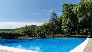 Piscina retangular com água azul cristalina, rodeada por um deck de pedra.