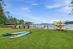 A grassy area with kayaks, a wooden deck, and a gazebo by a lake.