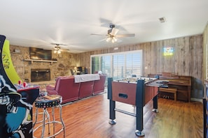 A living room with a foosball table, a red sofa, a stone fireplace, and a large window.
