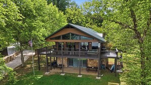 Ein zweistöckiges Haus mit Terrasse, Sitzgelegenheiten im Freien und einem Steinfundament.