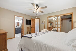 A bedroom with a bed, a ceiling fan, a wooden dresser, a mirror, and a door leading to a bathroom.