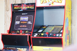 Des bornes d’arcade portant les inscriptions « Mortal Kombat » et « Pac-Man », avec un fond en bois.