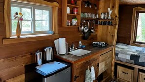 Interior de una cabaña de madera con kitchenette, una ventana con vistas y un estante con utensilios de cocina.
