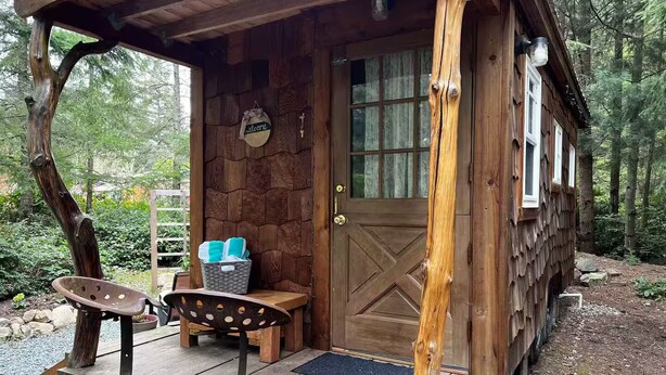 Una cabaña rústica con puerta de madera, un banco y una mesa en el exterior.