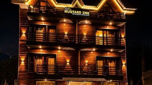 A two-story wooden building with balconies, labeled 'Mustard Inn,' featuring outdoor seating and a car parked nearby. - Hotel Mustard INN Pahalgam (Anantnag)