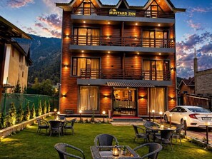 Un hotel de dos pisos con fachada de madera, balcones y mobiliario exterior.