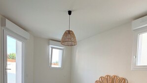 Ett sovrum med en säng, en sänggavel av rotting, en hängande lampa och utsikt över omgivningen.