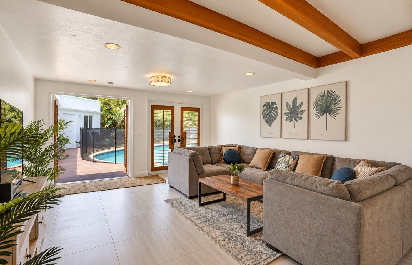 A spacious living room with a grey sofa, a coffee table, and a view of a swimming pool through glass doors.