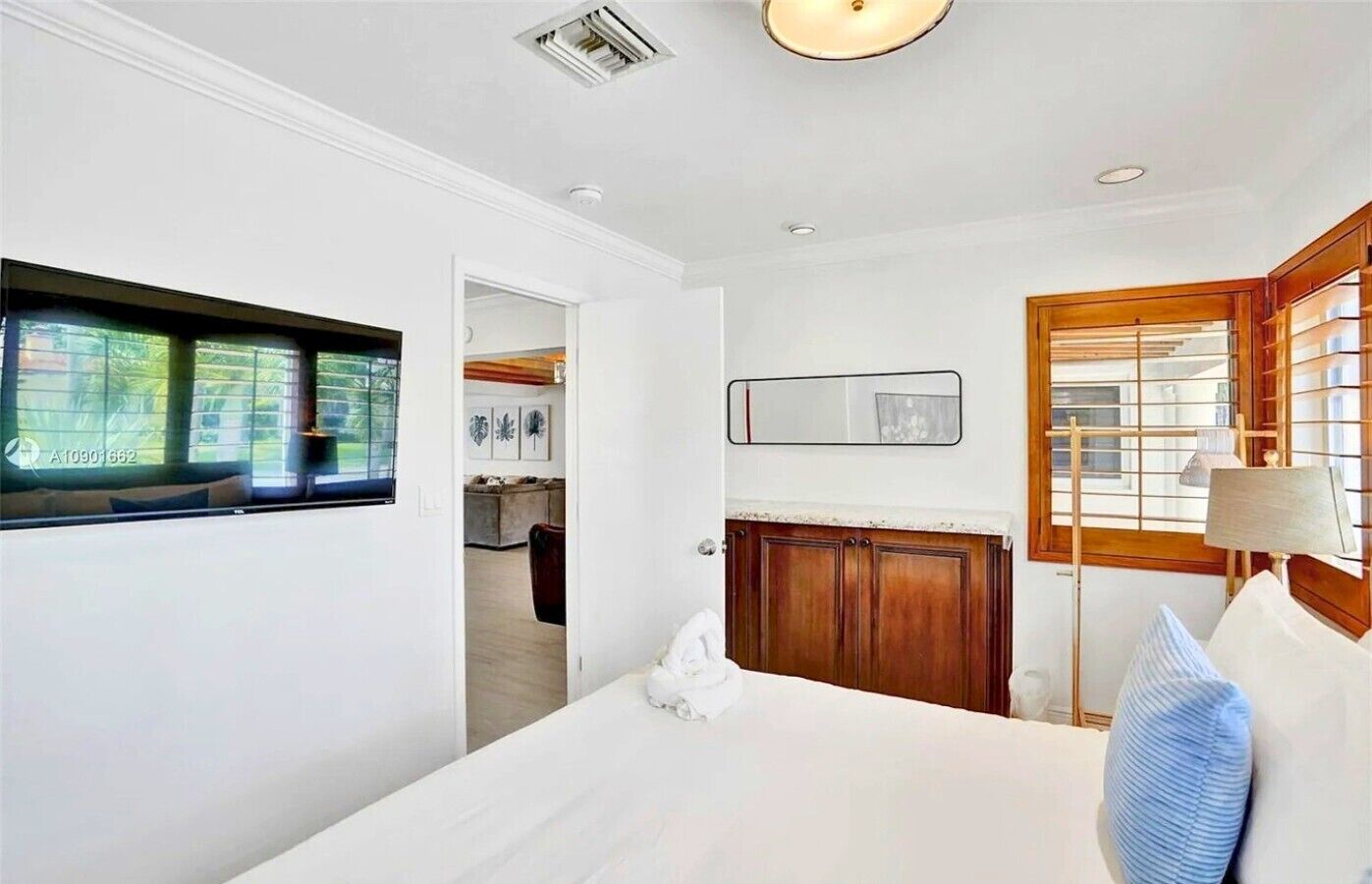 A bedroom with a large bed, a window, a mirror, and a wooden cabinet.