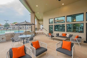An outdoor patio with seating, a grill, and a view of a swimming pool.