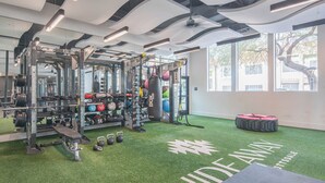 Uma academia com área de musculação, saco de pancada e piso de grama sintética verde.