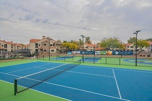 En tennisbane med net, omgivet af bygninger og et banner der reklamerer for 'Hideaway'.