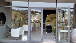 Un bâtiment moderne doté de grandes portes vitrées, d’un espace détente avec des chaises et une table, et offrant une vue sur un quartier résidentiel.